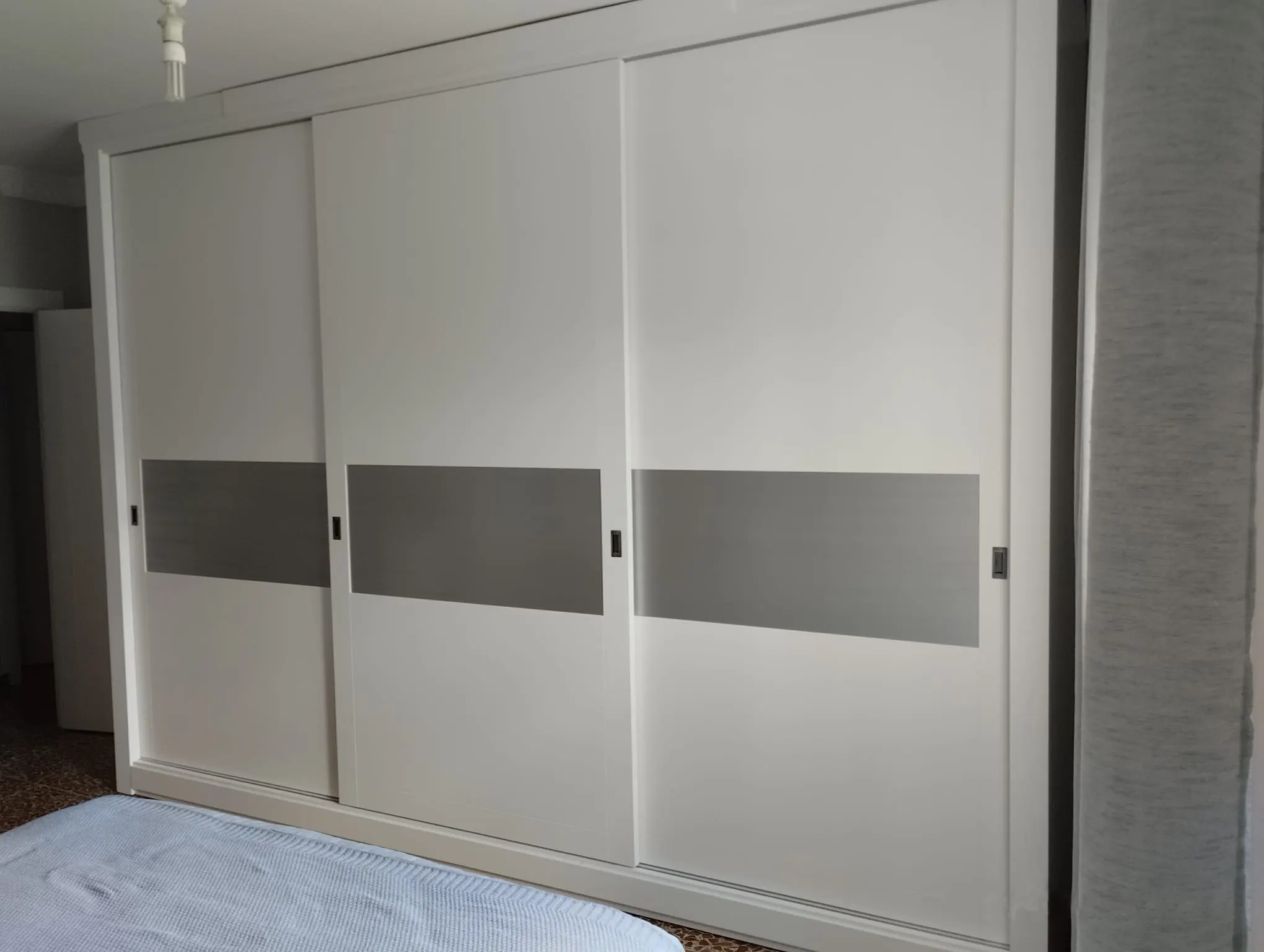 Armario empotrado de suelo a techo con tres puertas correderas blancas y una franja gris horizontal