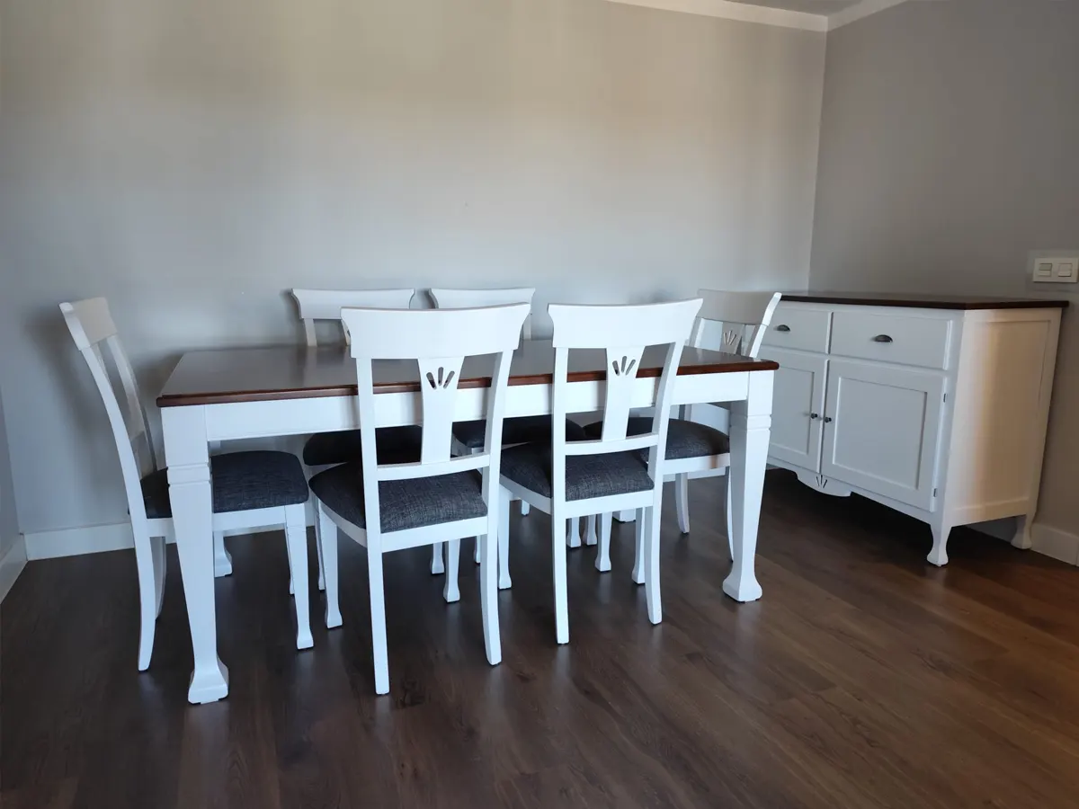 Mesa de comedor blanca con tablero de madera oscura, seis sillas tapizadas en gris y aparador a juego