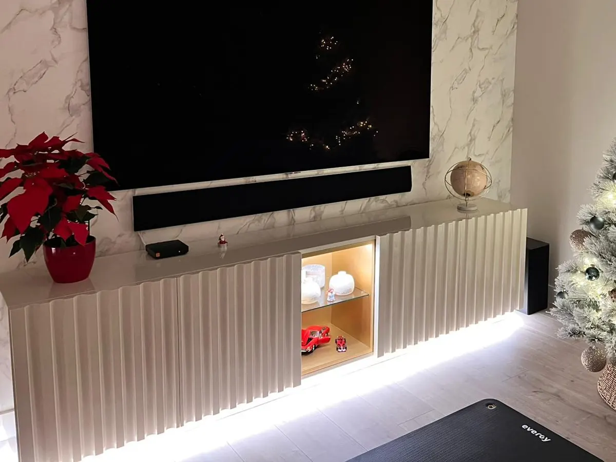 Mueble de TV volado lacado en tono claro con frentes ondulados, hornacina iluminada y luz LED inferior
